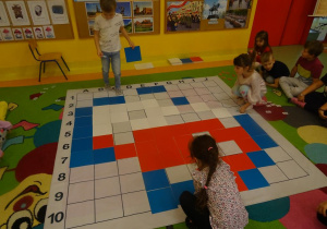 Troje dzieci układa na macie do kodowania kolorowe płytki zgodnie z wybranym kodem.